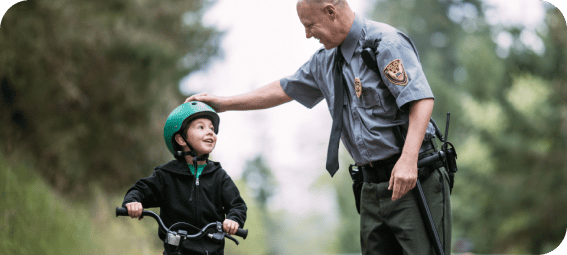 a policeman touching the helmet of a boy riding a bicycle