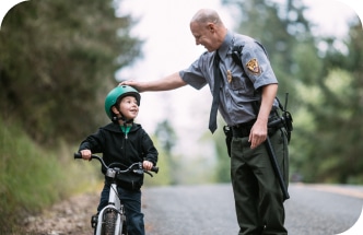 a policeman touching the helmet of a boy riding a bicycle